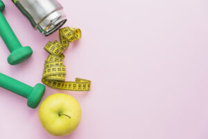 dumbbells-water-bottle-measuring-tape-and-apple-on-pink-background